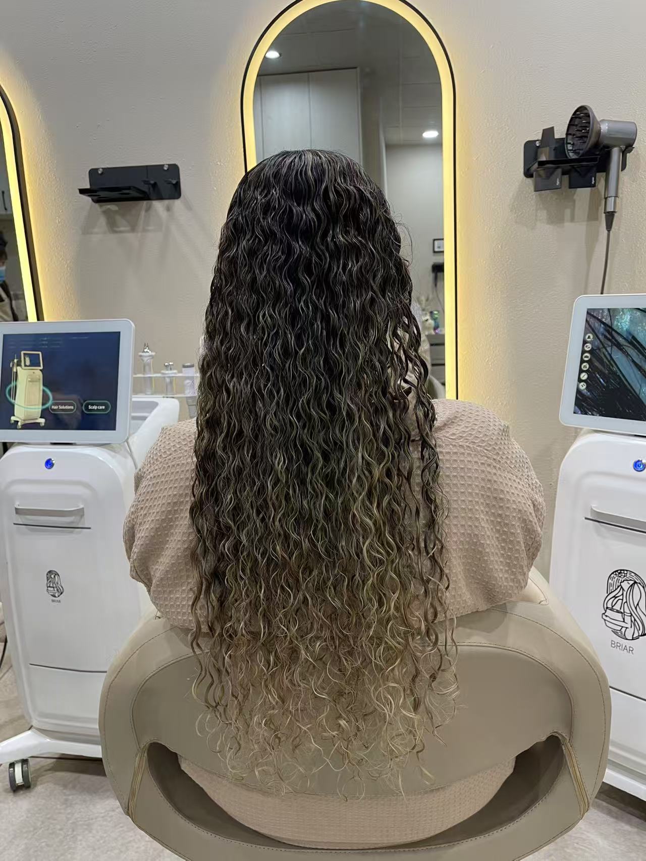 Long dark hair styled into defined spiral curls with blonde ends, finished at a lit-mirror styling station